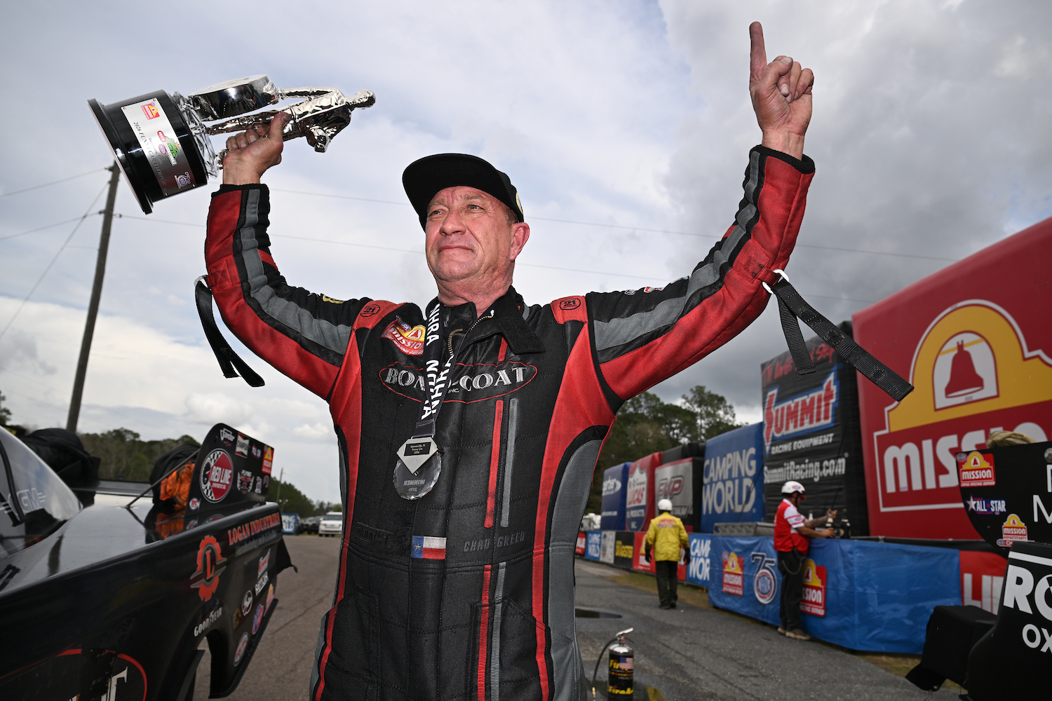Chad Green raises the trophy overhead, both arms up, in the Bond-Coat firesuit