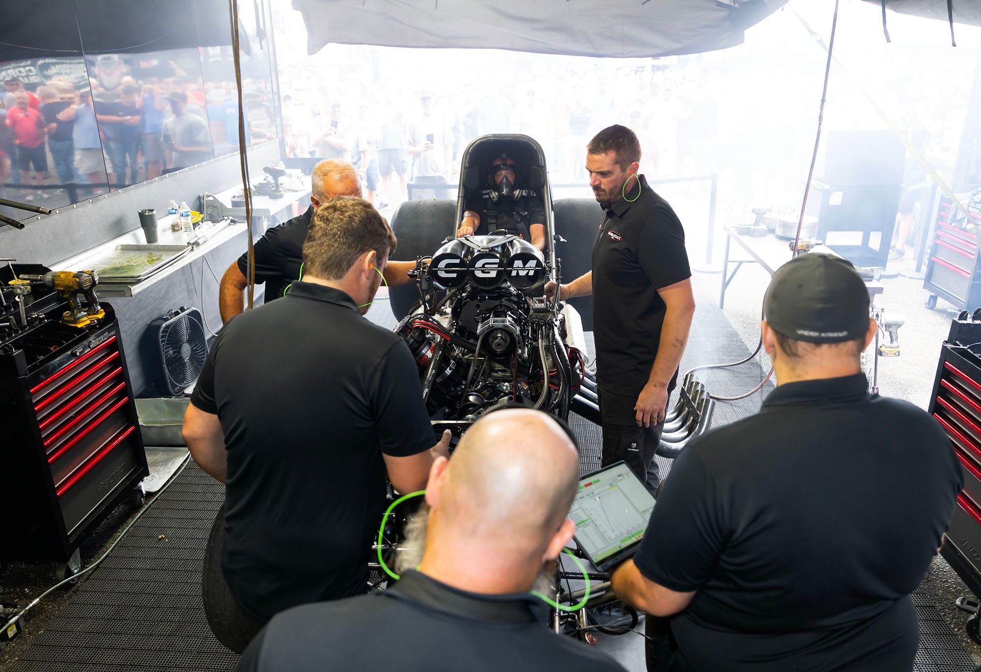 The crew gathers around the chassis for the warm-up under the pit awning