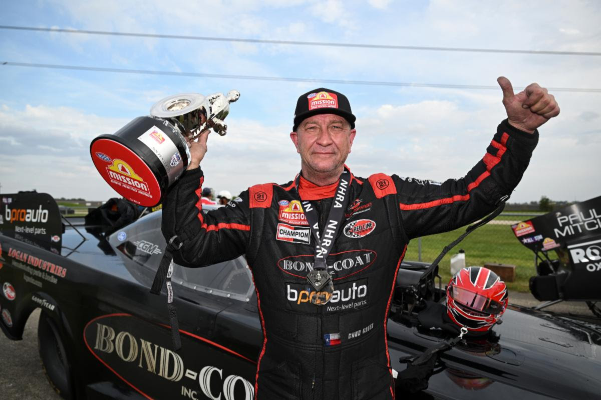 Chad Green in his firesuit holding the Wally trophy aloft beside the Bond-Coat Funny Car