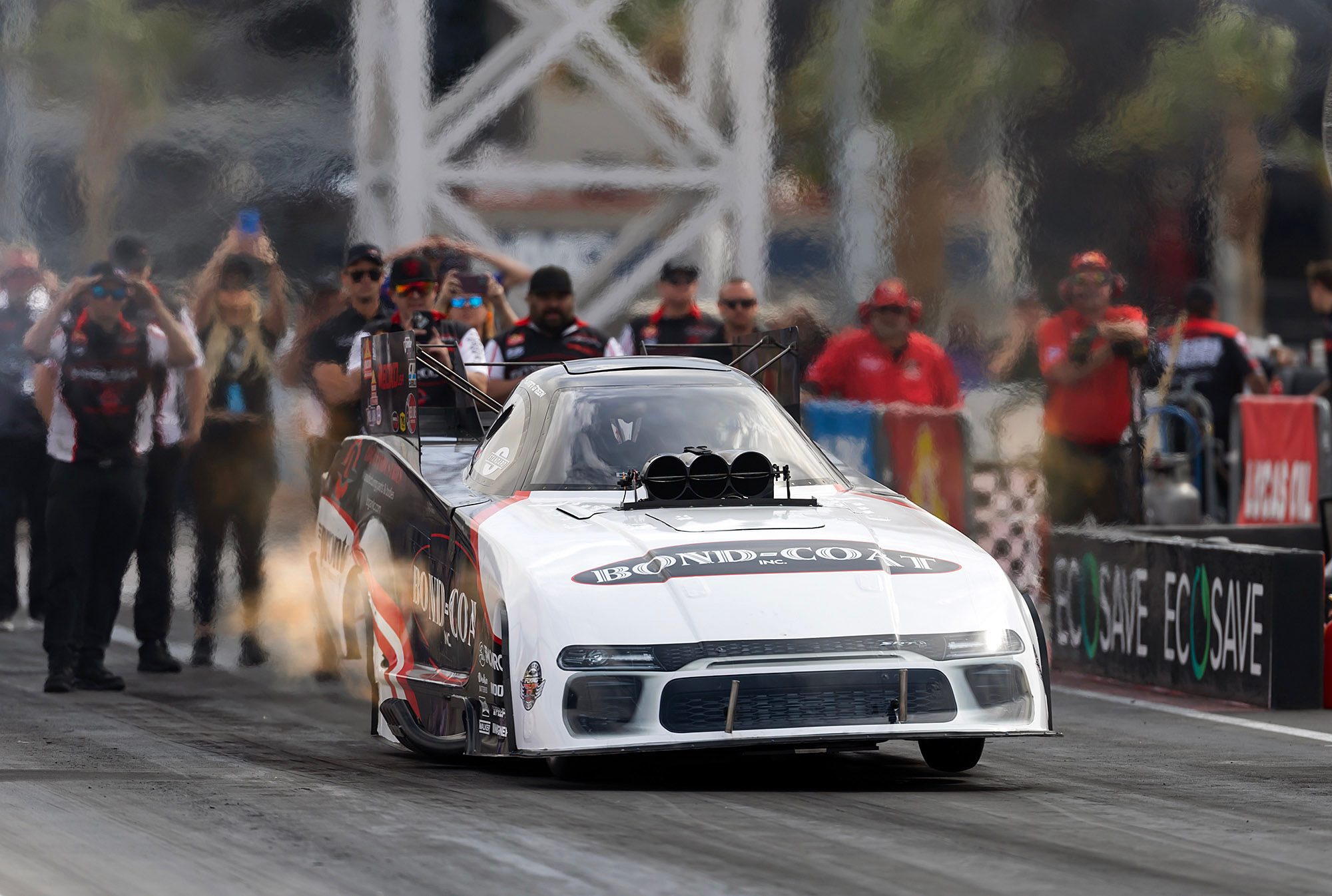 The white Bond-Coat Funny Car rolls through its burnout with the crew lined up behind
