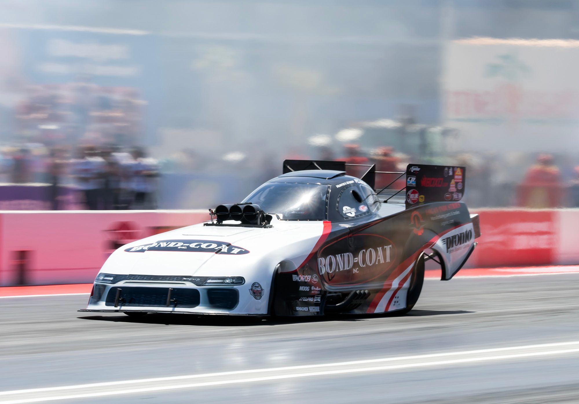 The white Bond-Coat Funny Car leaves the line with header flames in front of the grandstand