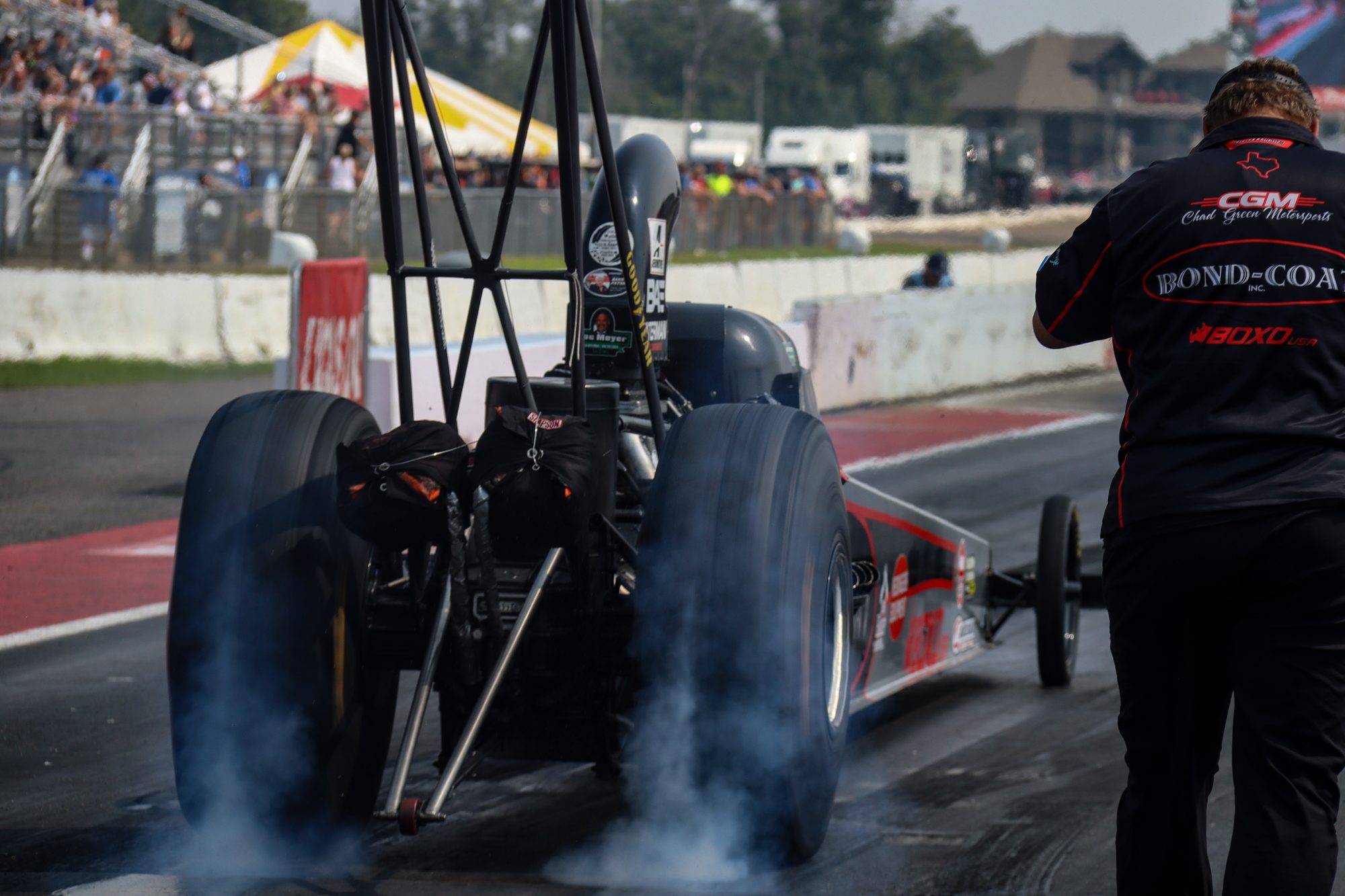 Hunter Green's dragster smokes the tires, a crew member watching from the wall