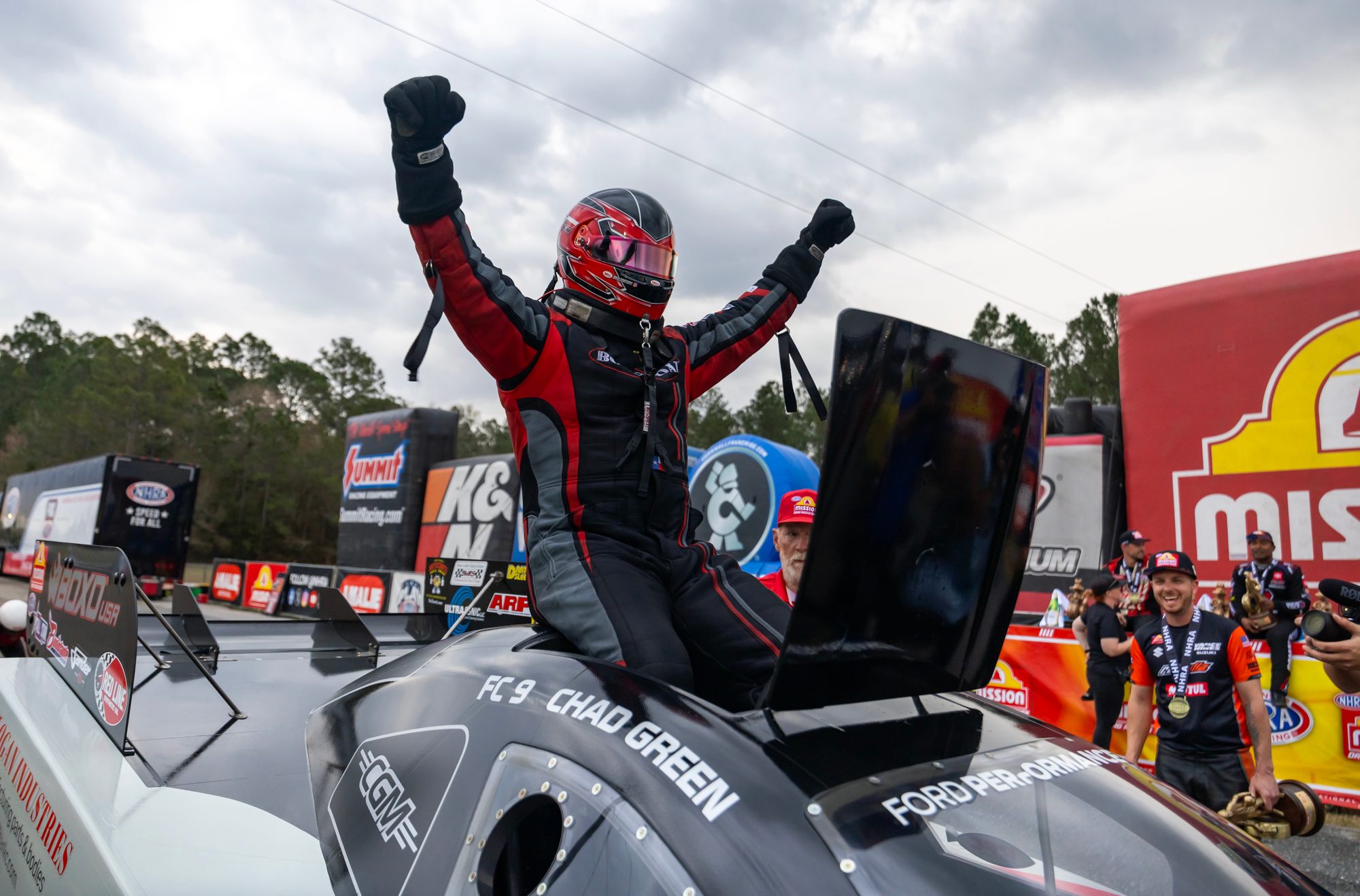 Chad Green climbs out and throws his arms up on the roof of the Funny Car