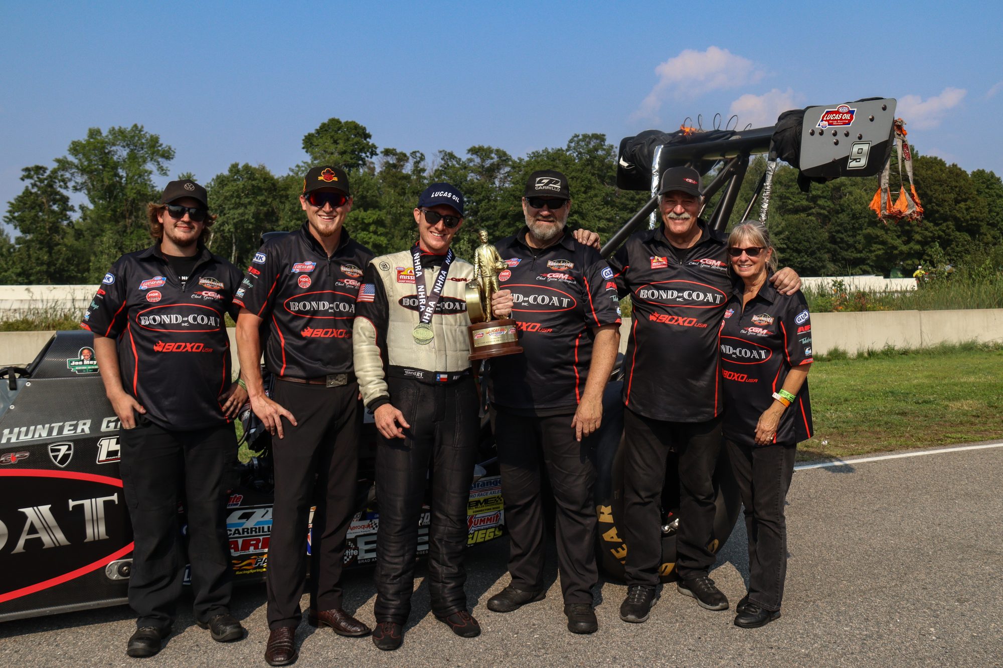 The team lines up with the trophy beside the dragster